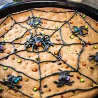 Chocolate chip baked in a cast-iron skillet and topped with decorated with a piped black spider web with piped spiders and sprinkles.