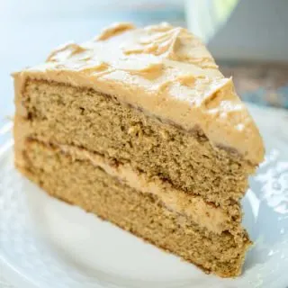 A piece of layered Spice Cake with Peanut Butter frosting between the layers and over the top on a white plate.
