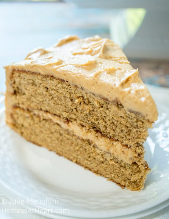 A piece of layered Spice Cake with Peanut Butter frosting between the layers and over the top on a white plate.