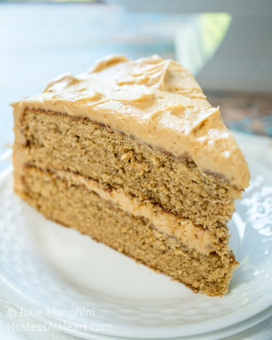 A piece of layered Spice Cake with Peanut Butter frosting between the layers and over the top on a white plate.