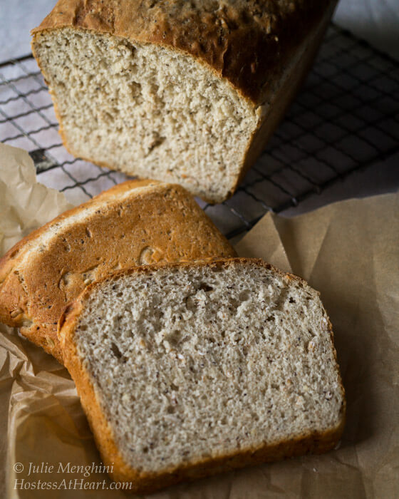 Top down view of two slices of Honey Whole Grain Bread sitting in front of the cut loaf sitting over a cooling rack.