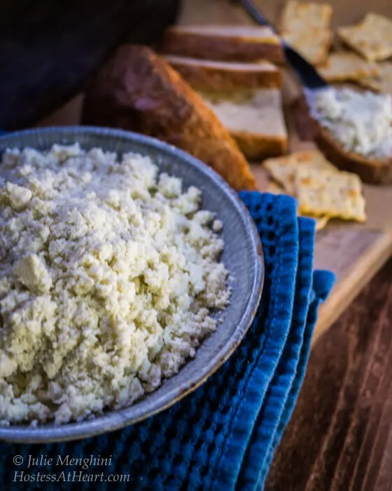 Blue bowl holding a cheese spread sitting next to serving crackers and sliced bread.