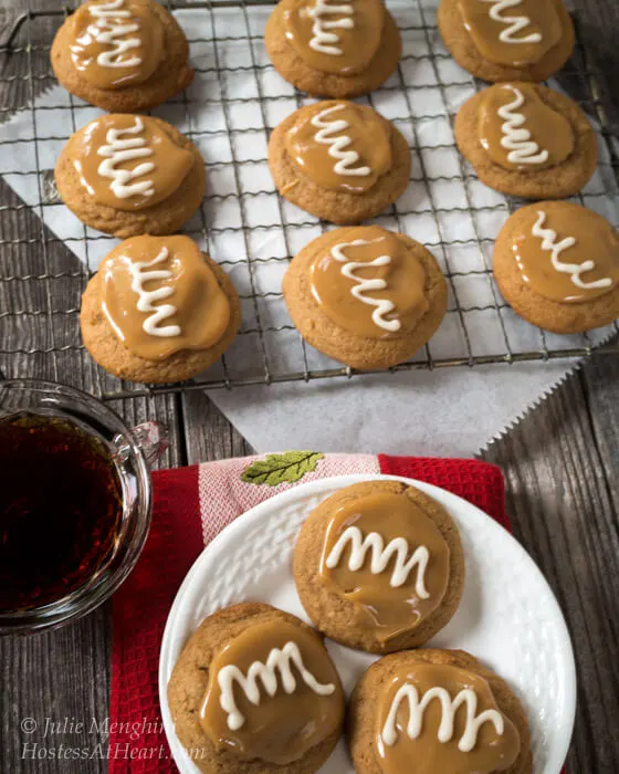 A white plate holding 3 Spiced Coffee Cookies that have a caramel topping with a white swirl. A cooling rack sits in the background full of cookies next to a cup of coffee.