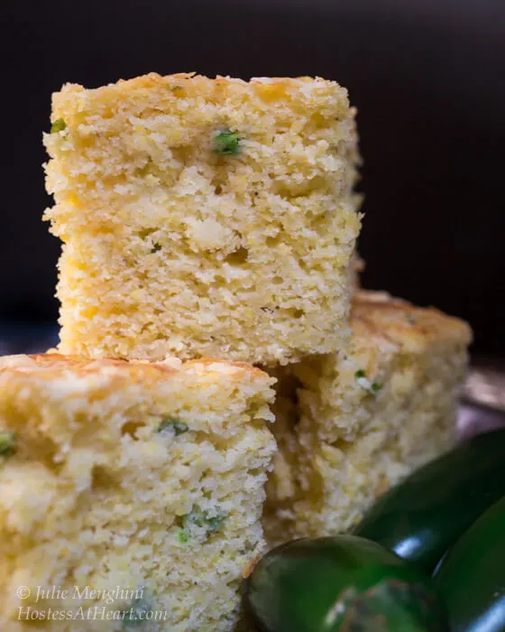 Three slices of Jalapeno Cheddar Cornbread surrounded by fresh jalapenos.