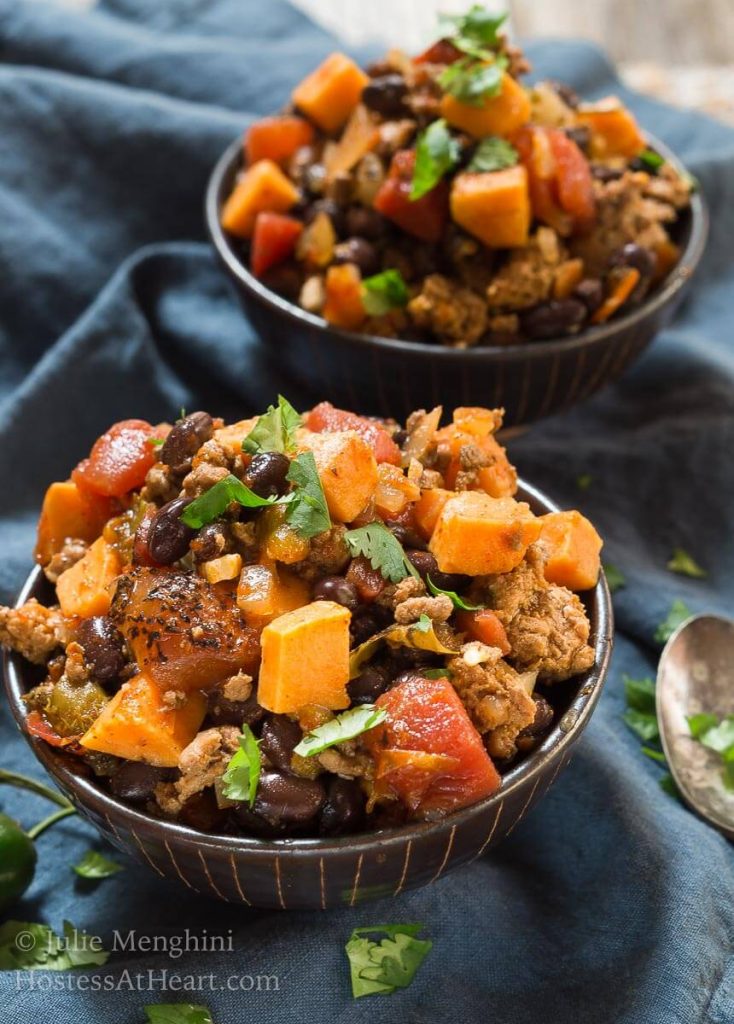 Two bowls of Sweet Potatoe and Black Been Chili sitting on a blue napkin.