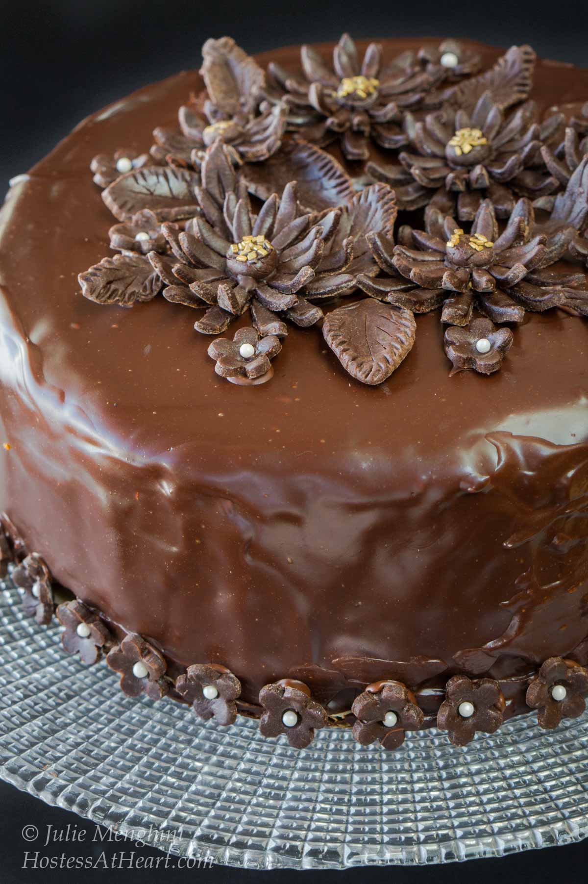 Beautiful round chocolate cake with a shiny ganache decorated with chocolate flowers.