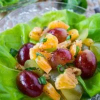 Butter lettuce leaf filled with a fruit salad made of grapes and clementines sitting on a glass plate.
