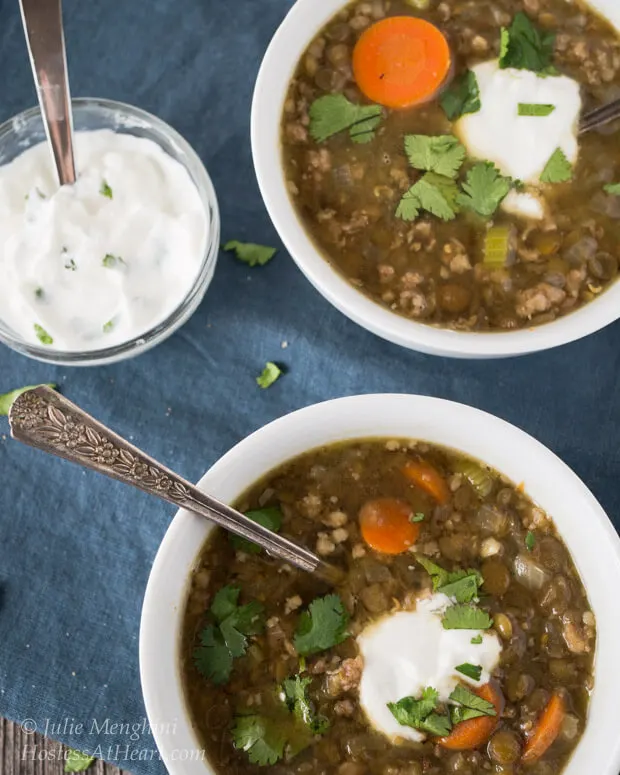 Two white bowls of Lentil sausage soup garnished with a dollop of sour cream.