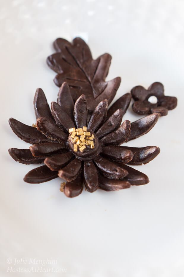 Model chocolate shaped into flowers and leaves garnished with gold sprinkles.