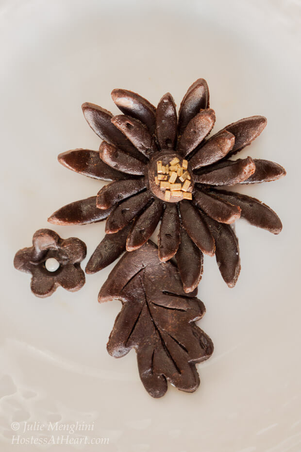 Model chocolate shaped into flowers and leaves garnished with gold sprinkles.