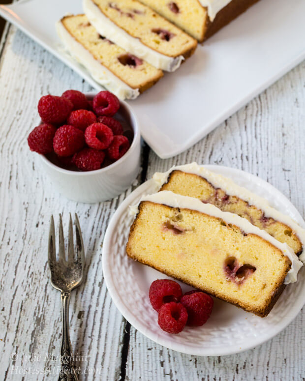 A white plate layered with slices of a Raspberry Pound Cake. A bowl of fresh raspberries sits to the side.