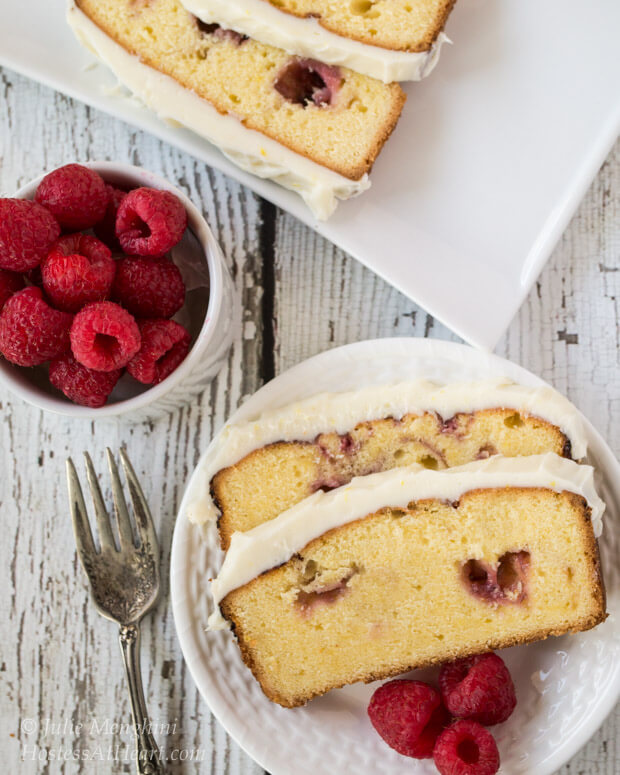 A white plate layered with slices of a Raspberry Swirl Pound Cake. A bowl of fresh raspberries sits to the side.
