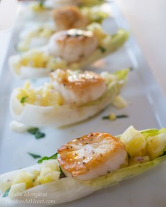 A row of endive leaves filled with scallops and pineapple salsa sitting on a white tray.