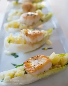 A row of endive leaves filled with scallops and pineapple salsa sitting on a white tray.