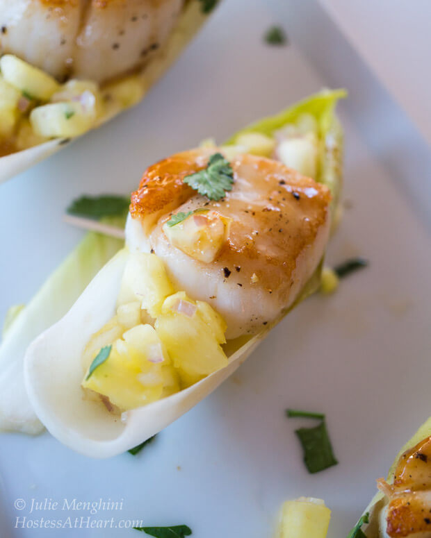 Endive lettuce holding a cooked scallop and pineapple salsa on a white plate.