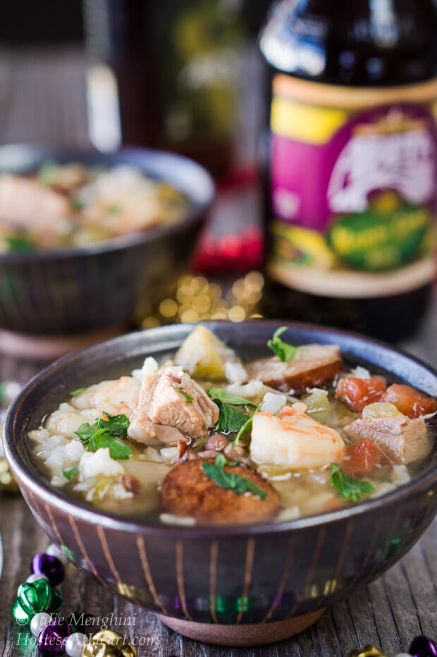 Two bowls of shrimp duck sausage gumbo in a brown bowl with a beer in the background surrounded by beads for Mardi Gras.