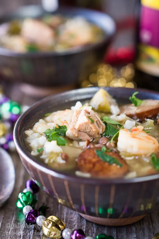 Large pieces of duck, sausage and shrimp  sit in a spicy broth with colorful Mardi Gras beads surrounding the bowl.