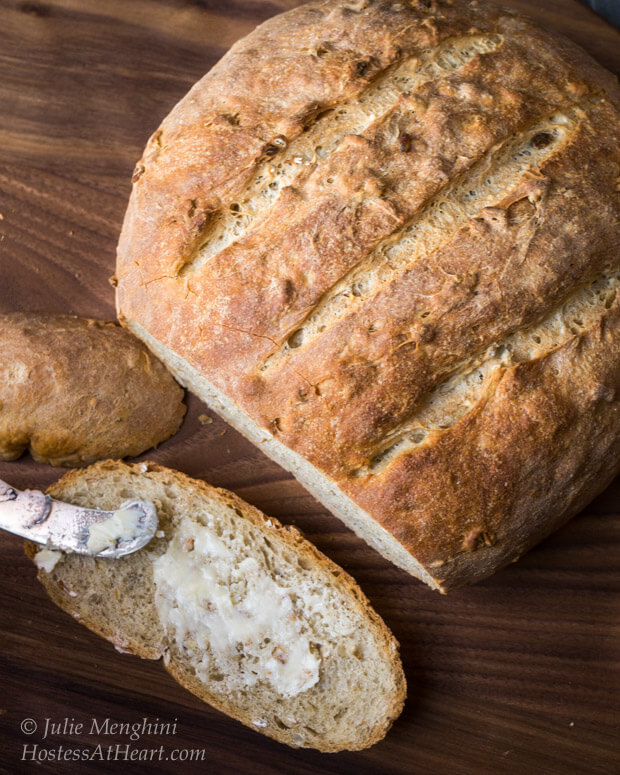 A loaf of bread with the first slice sitting in the front that\'s been buttered.