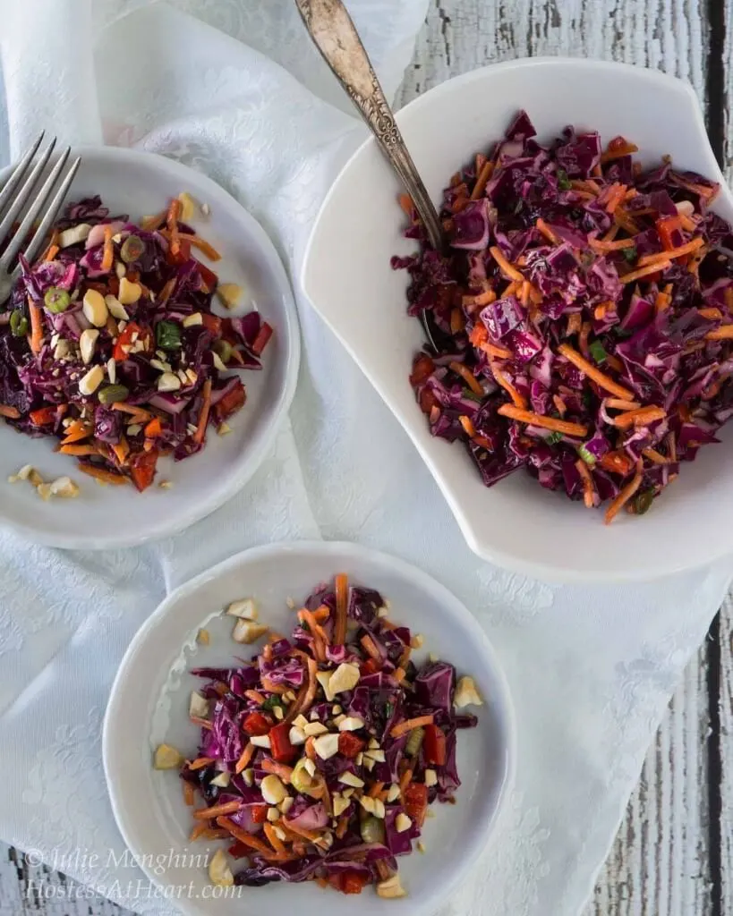 Purple cabbage salad sitting on a white plate and garnished with chopped nuts.