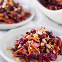 Purple cabbage salad sitting on a white plate and garnished with chopped nuts.