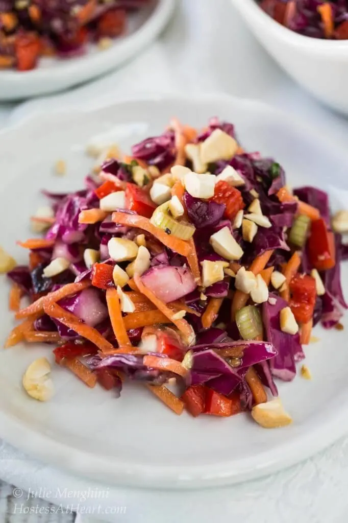 Chopped purple cabbage filled with diced red pepper and carrot sticks garnished with chopped cashews and dressed in a ginger sesame vinaigrette sits on a white bowl.