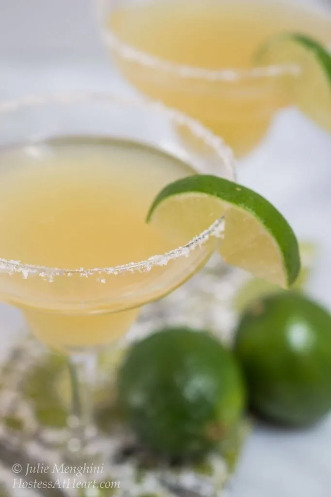 Two margarita glasses rimmed with salt and filled with margaritas. Two fresh limes sit in the front.