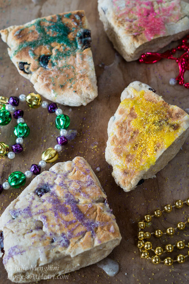 Slices of scones decorated with colored sugar with colored beads sitting in the front for Mardi Gras.