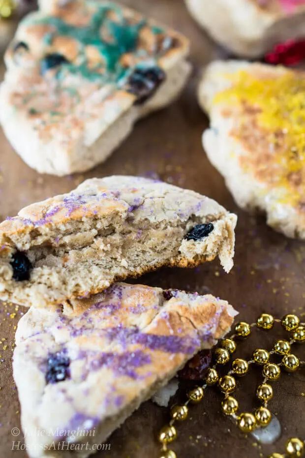 Slices of scones decorated with colored sugar with gold beads sitting in the front for Mardi Gras.
