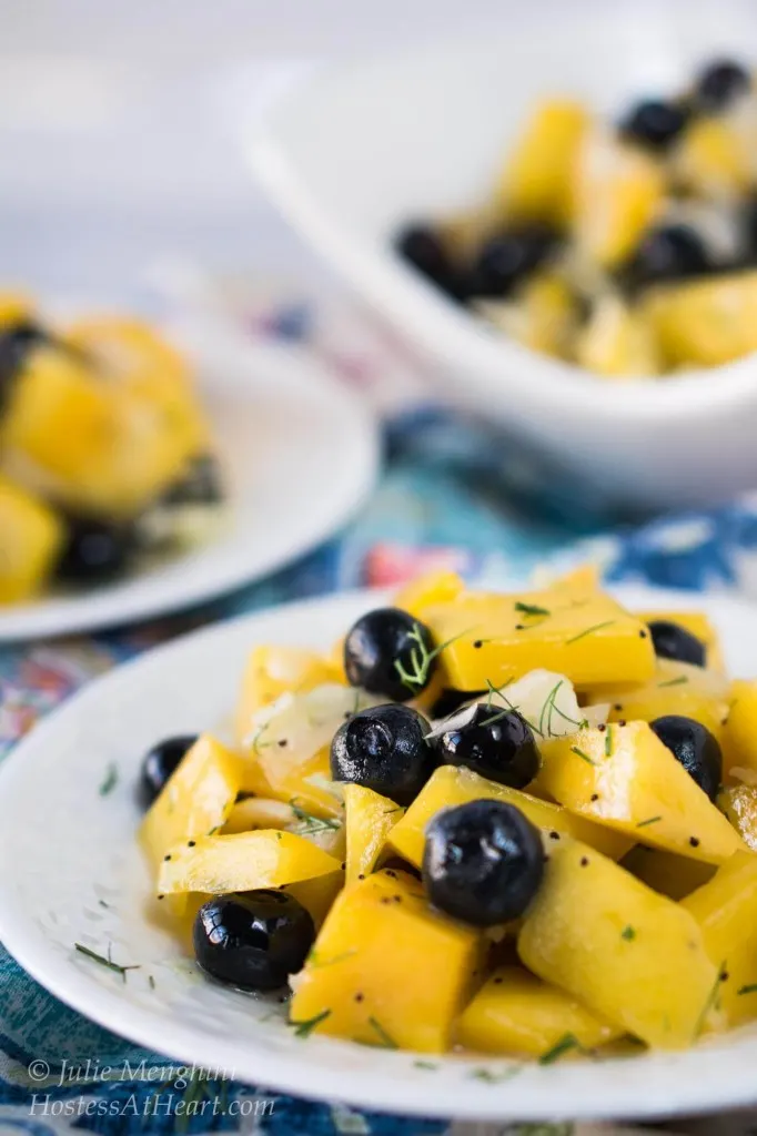 A white plate filled with a salad containing cubed mango, blueberries, and fennel and garnished with fennel fronds