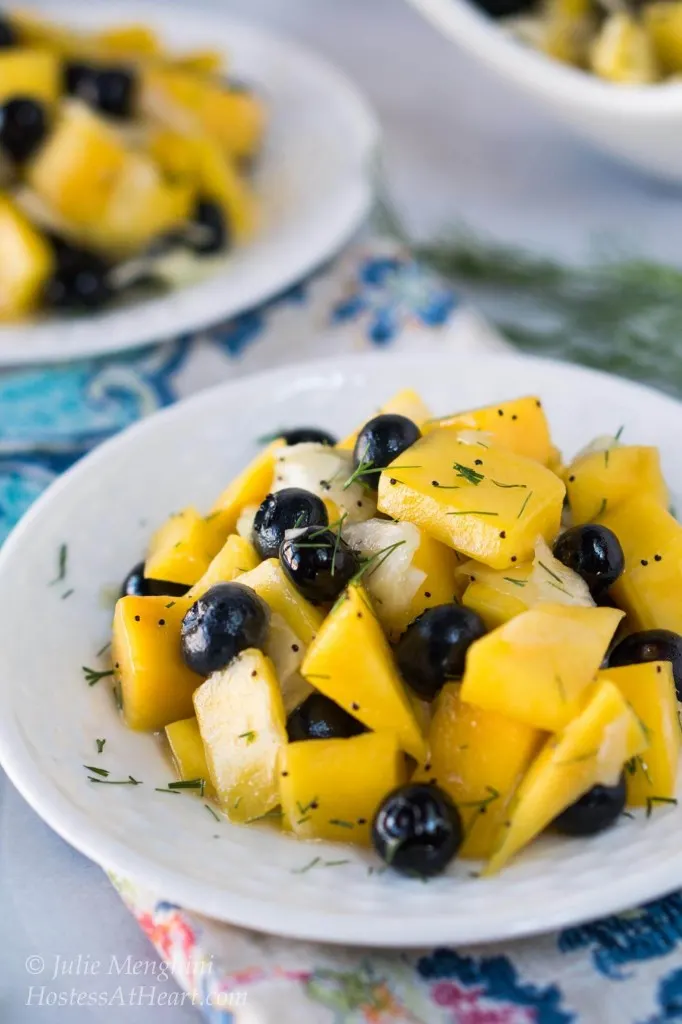White plate filled with slices of mango, blueberries, and fennel.
