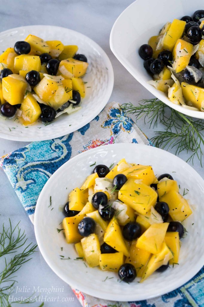 A white plate filled with a salad containing cubed mango, blueberries, and fennel and garnished with fennel fronds