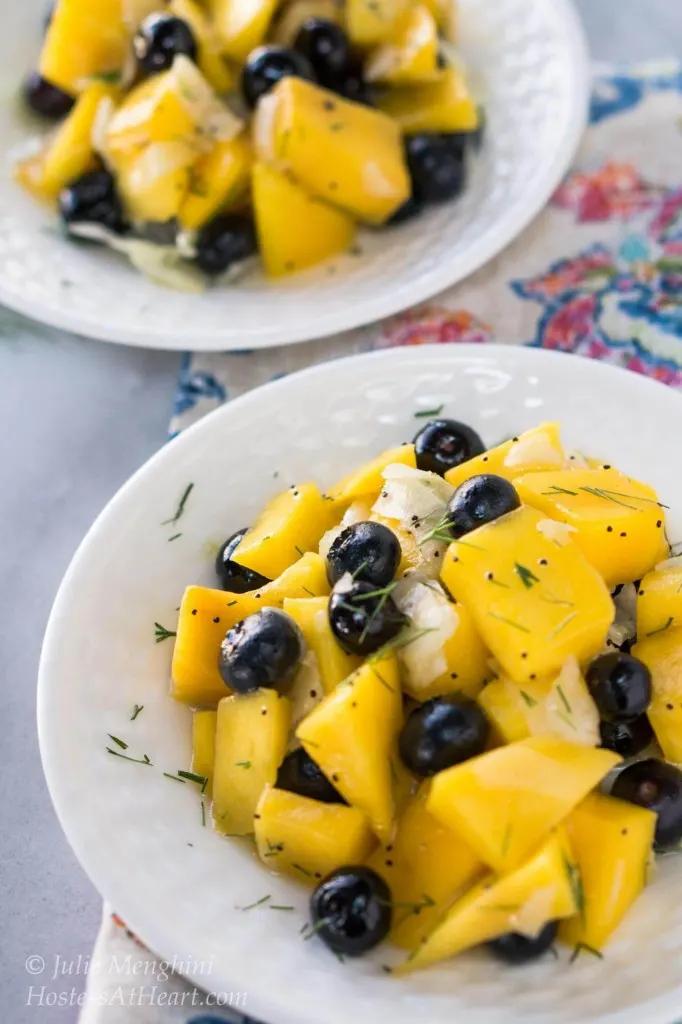 A white plate filled with a salad containing cubed mango, blueberries, and fennel and garnished with fennel fronds