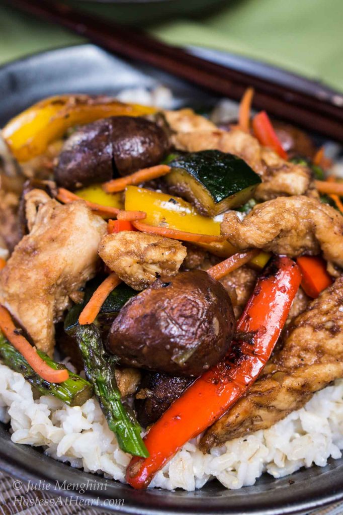 A bowl of white rice topped with chicken and vegetable stirfry.