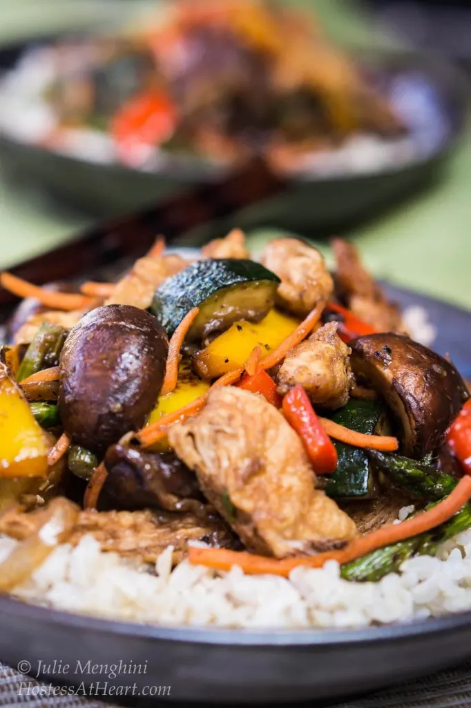 A bowl of white rice topped with chicken and vegetable stirfry.