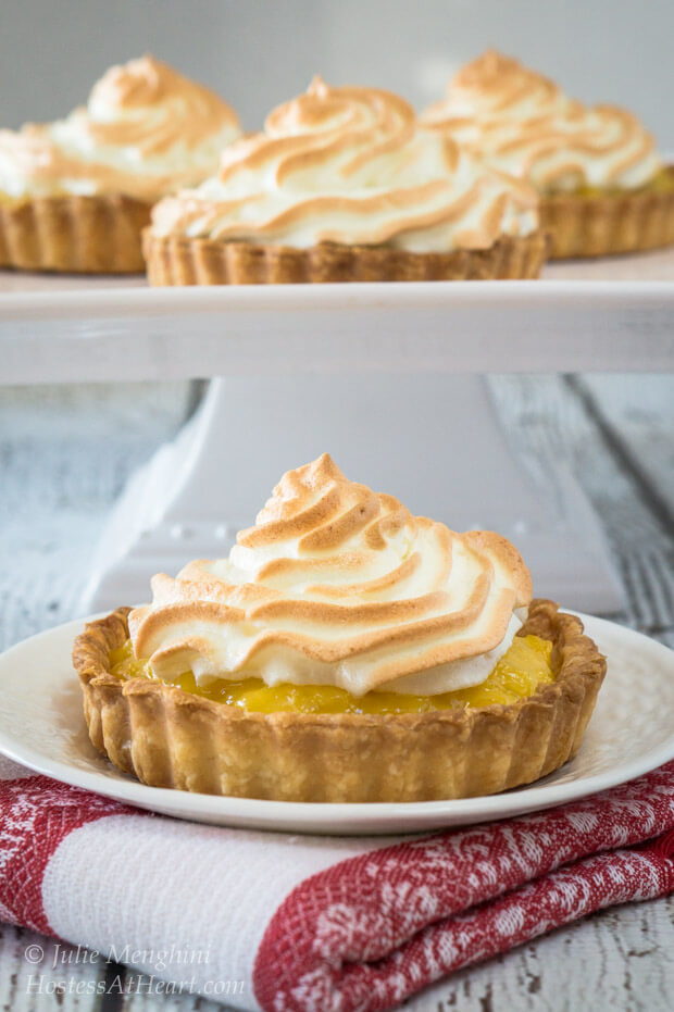 Pineapple Meringue Tart sitting on a white plate with a cake stand with more tarts in the background.