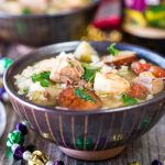 A bowl of Shrimp, Duck and Andouille Gumbo garnished with fresh parsley in a stiped bowl with New Orleans beads spread around it.