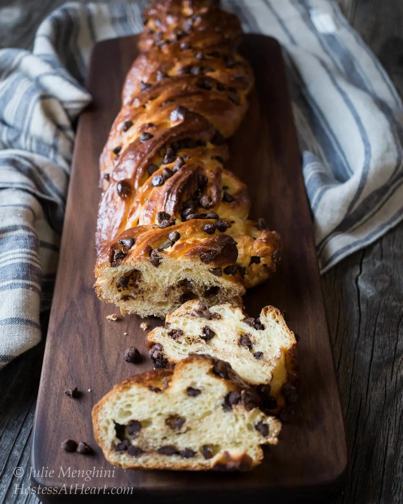 A braided chocolate bread on a bread wooden cutting board over a blue striped towel