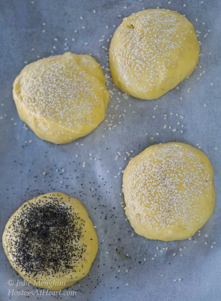 Top-down view of brioche bun dough sitting on a piece of parchment paper garnished with sesame seed or poppyseed.