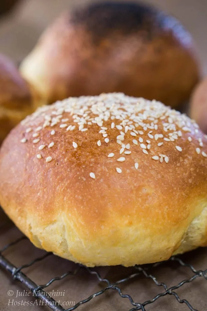 A closeup view of a brioche bun topped with sesame seeds. More buns sit in the background.