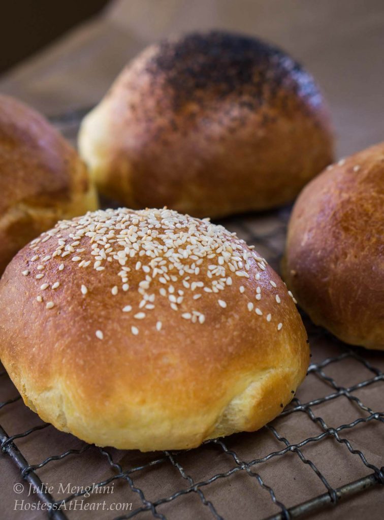 Angled view of brioche buns over a cooling rack and topped with sesame seeds or poppy seeds. Some are left plain.