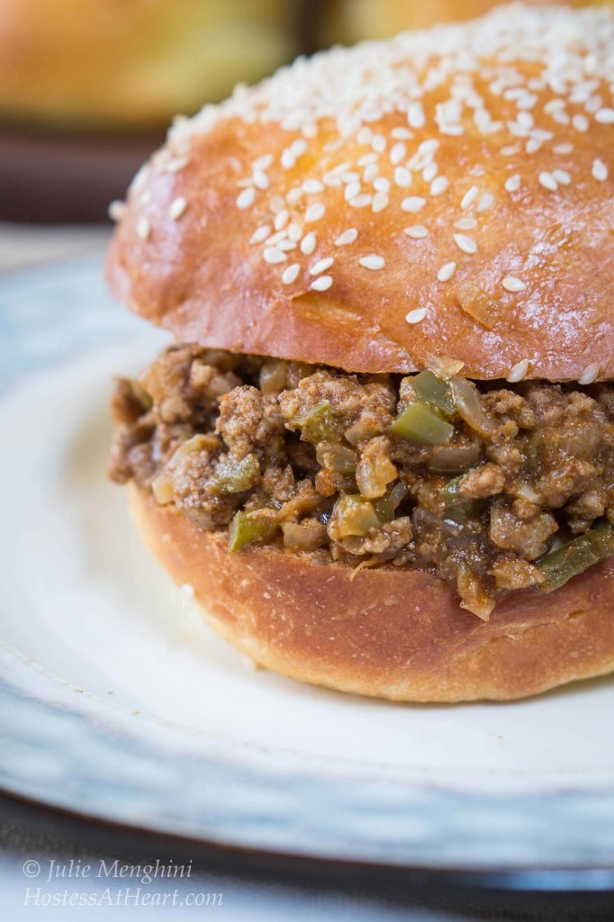 A side view of a sloppy joe sandwich made with turkey and dotted with green peppers on a sesame bun over a light blue plate.