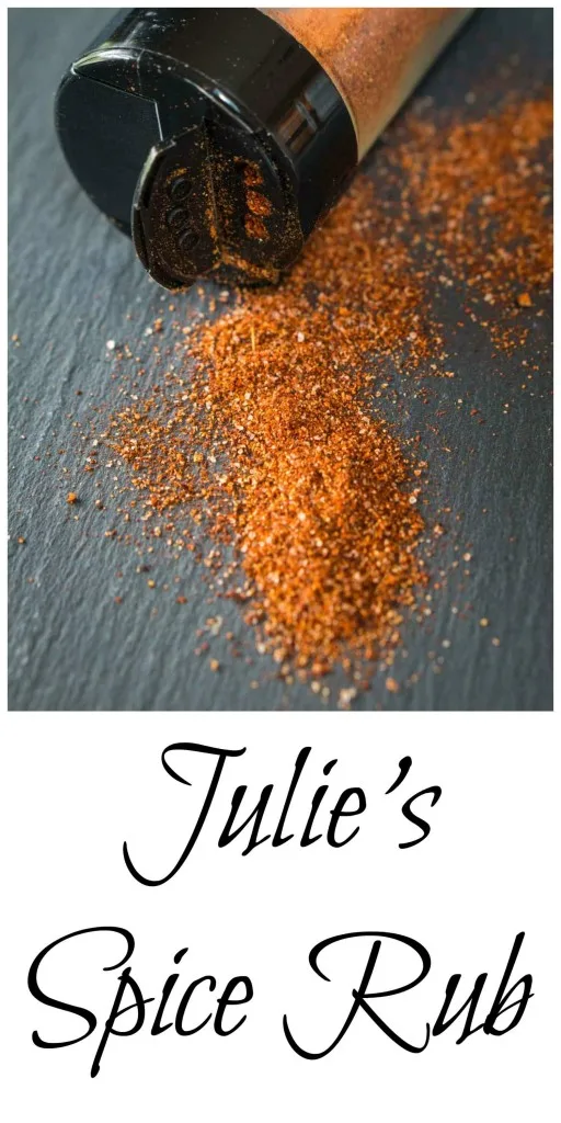 A spice jar laying on its side with the cap open and the spice rub spilling out on a piece of slate. The title \"Julie\'s Spice Rub runs across the bottom.