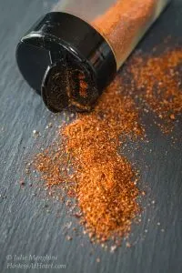 A spice jar sitting on it\'s side with a homemade spice rub spilling out over a piece of slate.