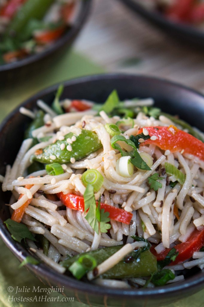 Top-down photo of a black bowl filled with soba noodles with Asian flavors stuffed with red peppers and garnished with sesame seeds and cilantro. A second bowl sits in the background.