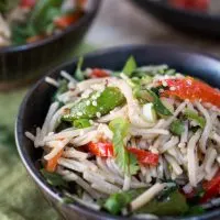 A black bowl filled with soba noodles with Asian flavors stuffed with red peppers and garnished with sesame seeds and cilantro. A second bowl sits in the background.