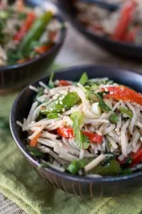 A bowl Soba Noodles, red peppers, green onions, and pea pods sitting over a green napkin with another bowl in the background. 