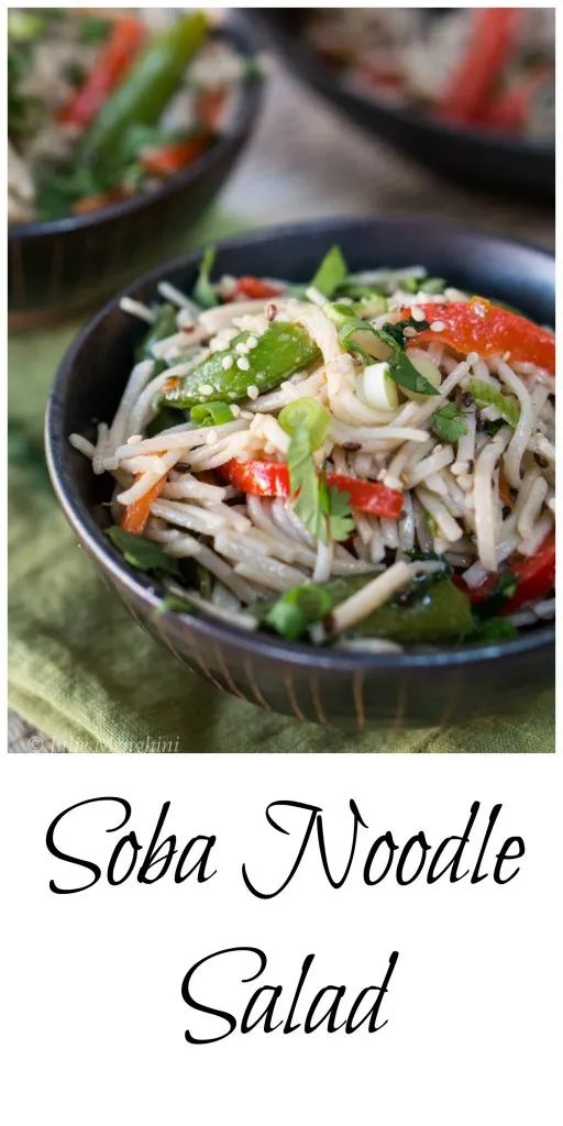 A black bowl filled with a soba noodle salad containing red peppers, green onions, and snap peas.