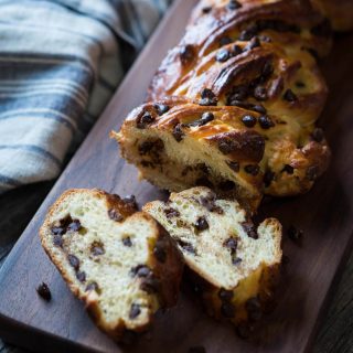 A braided chocolate bread on a bread wooden cutting board over a blue striped towel