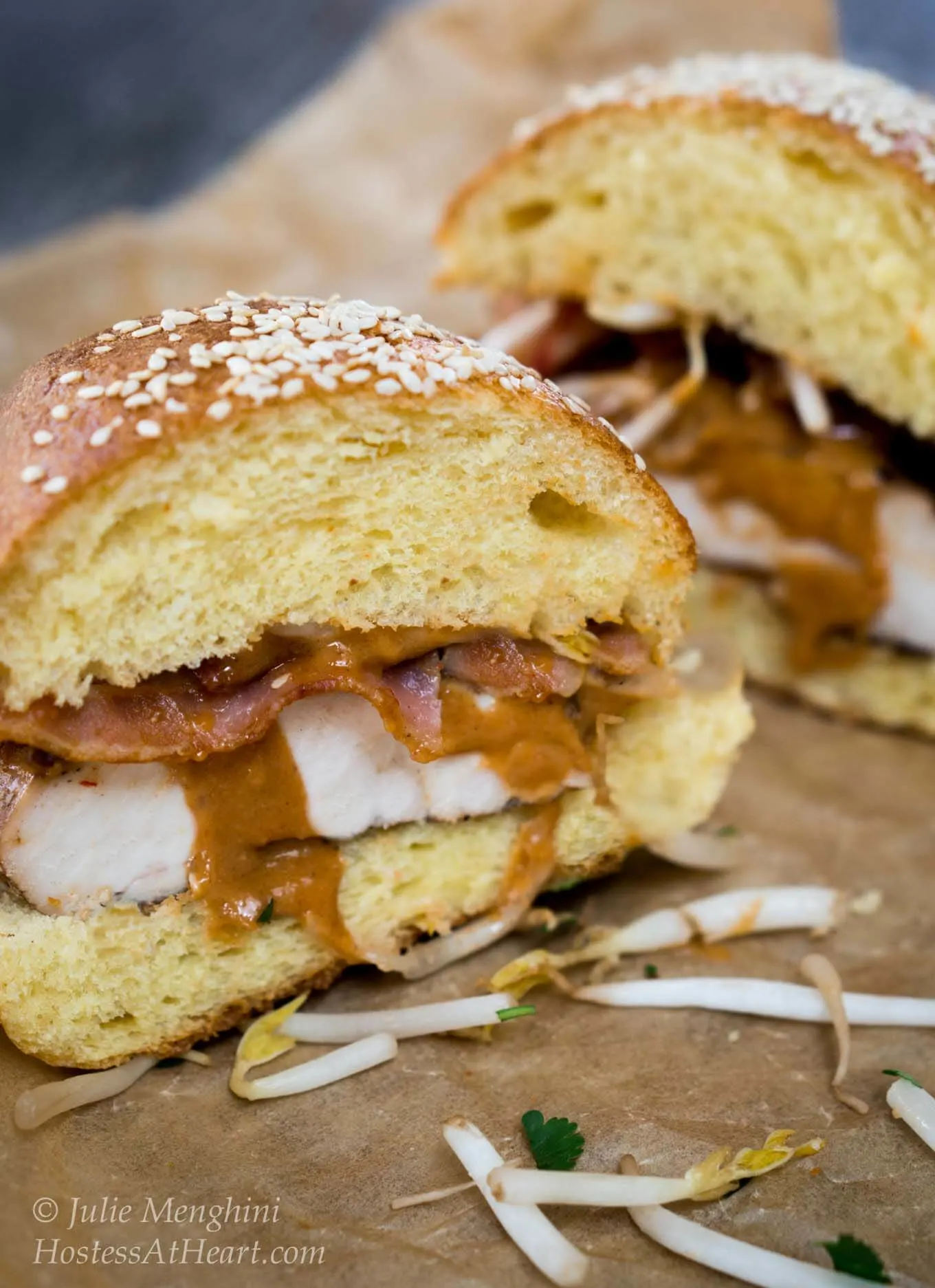 Two halves of a chicken sandwich layered with peanut sauce and bacon on a brioche bun.