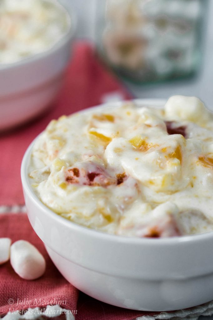 A whipped cream salad filled with fruit cocktail and cherries in a white bowl on top of a pink napkin